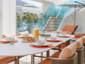 A modern dining area with a white table, orange placemats, and a glass of orange juice. - Exclusive penthouse with sea view in La Caleta (La Caleta)
