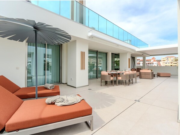 A modern outdoor living area with a sofa, a dining table, and a large umbrella. - Exclusive penthouse with sea view in La Caleta (La Caleta)