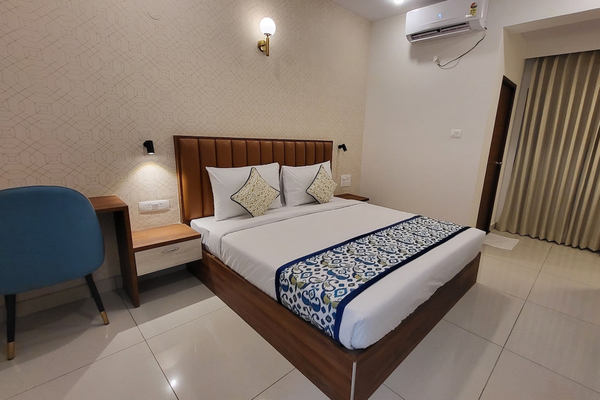 A hotel room with a bed, a nightstand, a chair, a wall-mounted air conditioner, and a window with curtains.