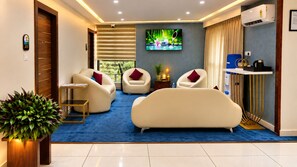 A modern hotel room with a large TV, comfortable seating, a small table, and a potted plant. - The Dritan Brookefield ITPL Main Road (Bengaluru)