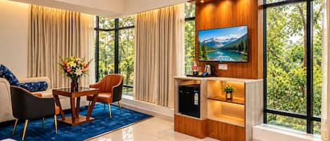 A modern living room with a large TV, a coffee machine, and a small fridge.