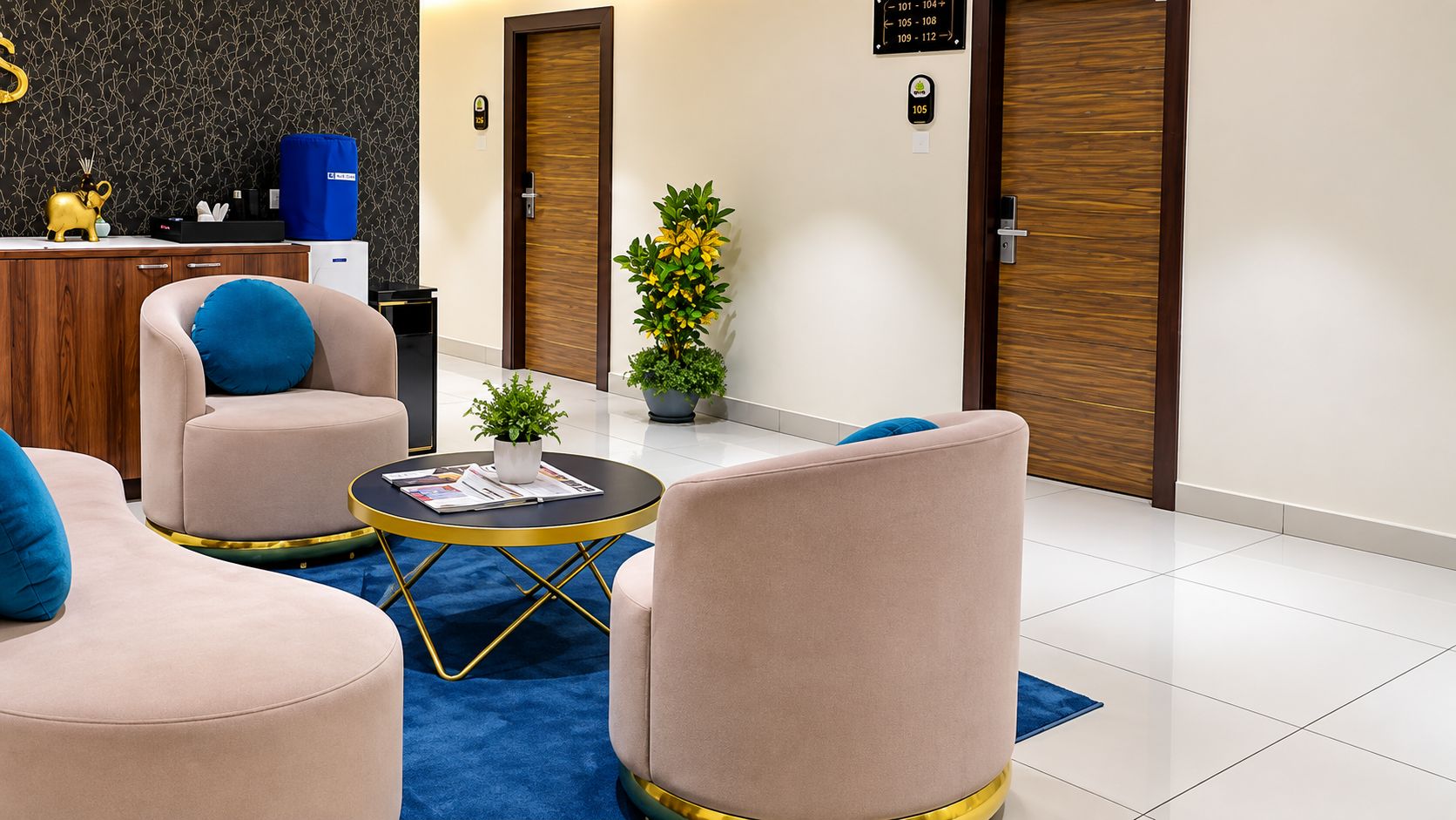 A modern hotel lobby with a reception desk, seating area with armchairs and a coffee table, and a potted plant.