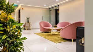 A modern interior with a seating area featuring pink chairs and a small table, a trash bin, and a fire extinguisher. - The Dritan Brookefield ITPL Main Road (Bengaluru)
