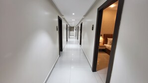 Un pasillo de hotel con paredes blancas, piso de baldosas y puertas que dan a las habitaciones.
