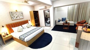 Habitación de hotel con cama, mesita de noche, armario y zona de estar con sofá y sillones.