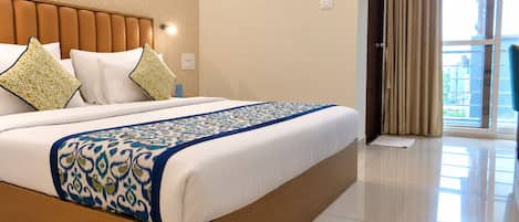 A hotel room with a large bed, a wooden headboard, and a view of the outdoors through a window.