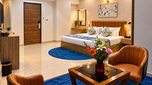 Une chambre d’hôtel avec un lit, un bureau, une chaise, un vase de fleurs et un tapis bleu.