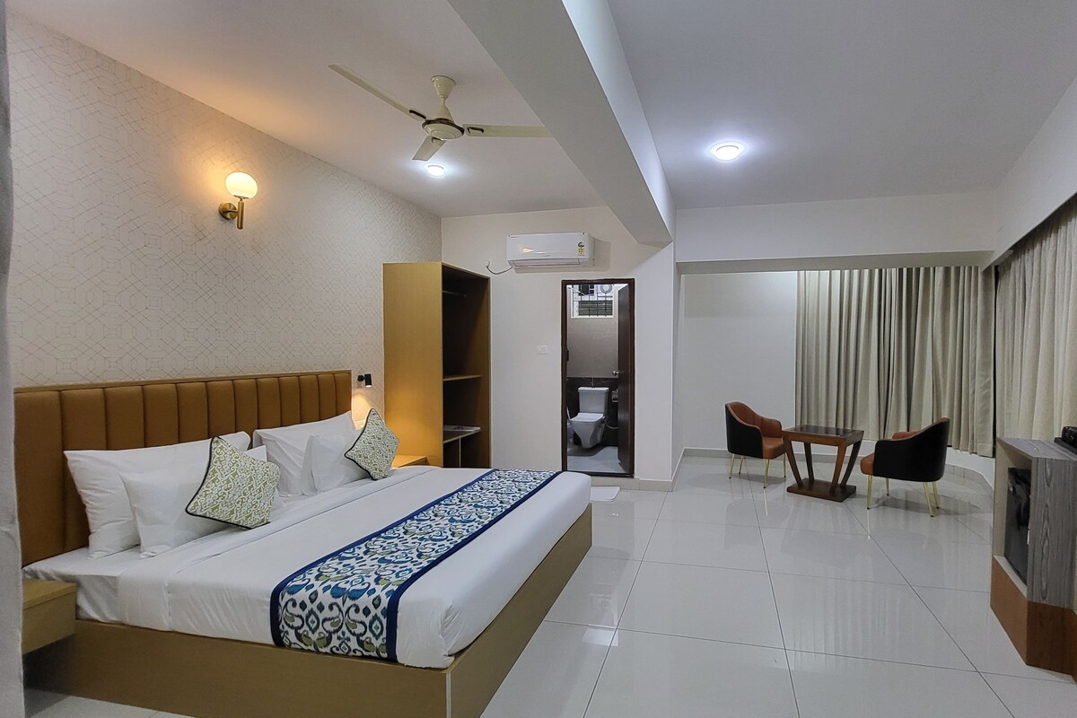 A hotel room with a bed, a desk, a chair, a TV, and a bathroom visible through an open door.