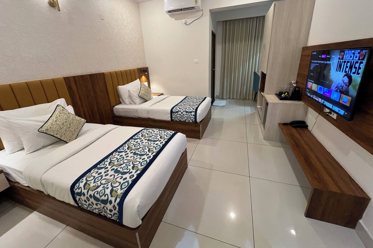 A hotel room with two beds, a TV, a desk, and an air conditioning unit.