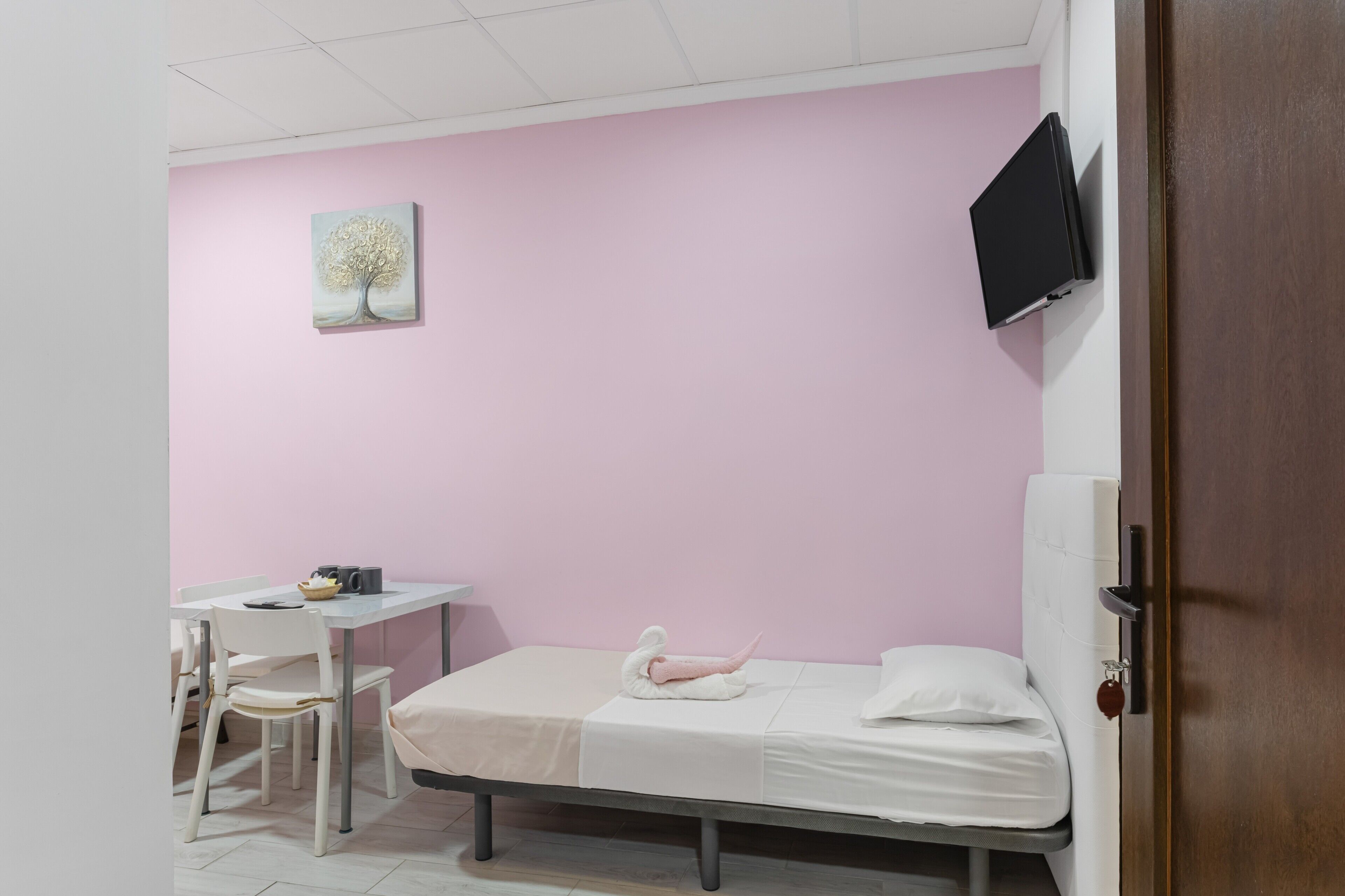 A room with a bed, a desk, a chair, a TV, and a painting on the wall.