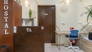 Ein Hotel-Rezeptionsbereich mit einem hölzernen Empfangstresen mit der Aufschrift 'HOSTAL', einem blauen Bürostuhl, einem Holztisch und einer Tür mit einem Schild.