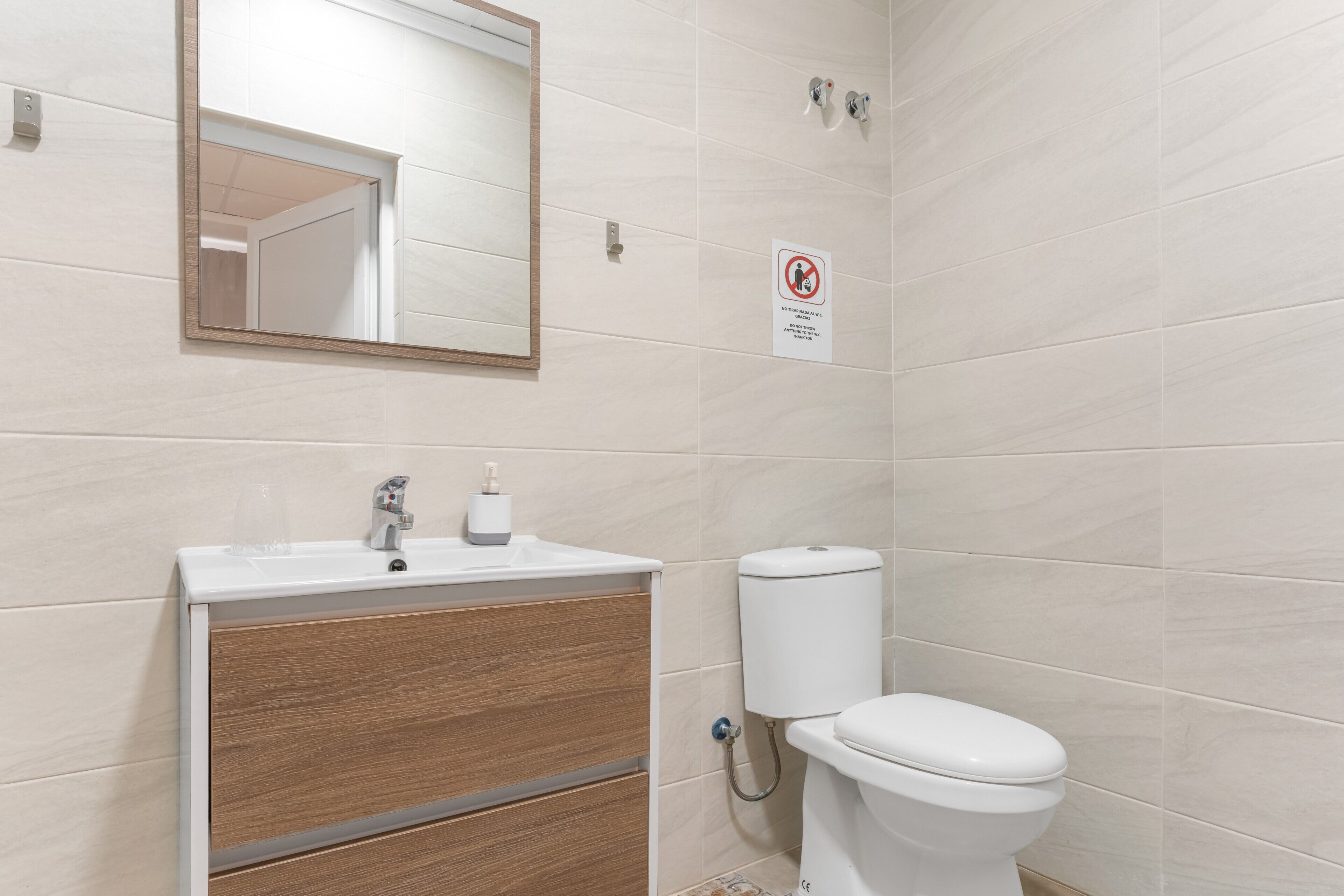 Un baño con lavamanos, espejo, inodoro y un cartel de prohibido fumar.