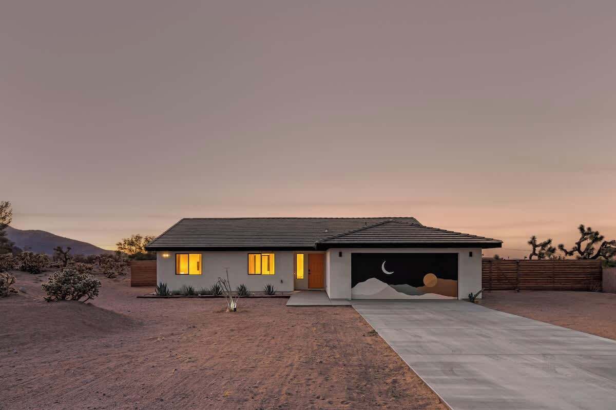 A modern house with a garage, a driveway, and desert landscaping.