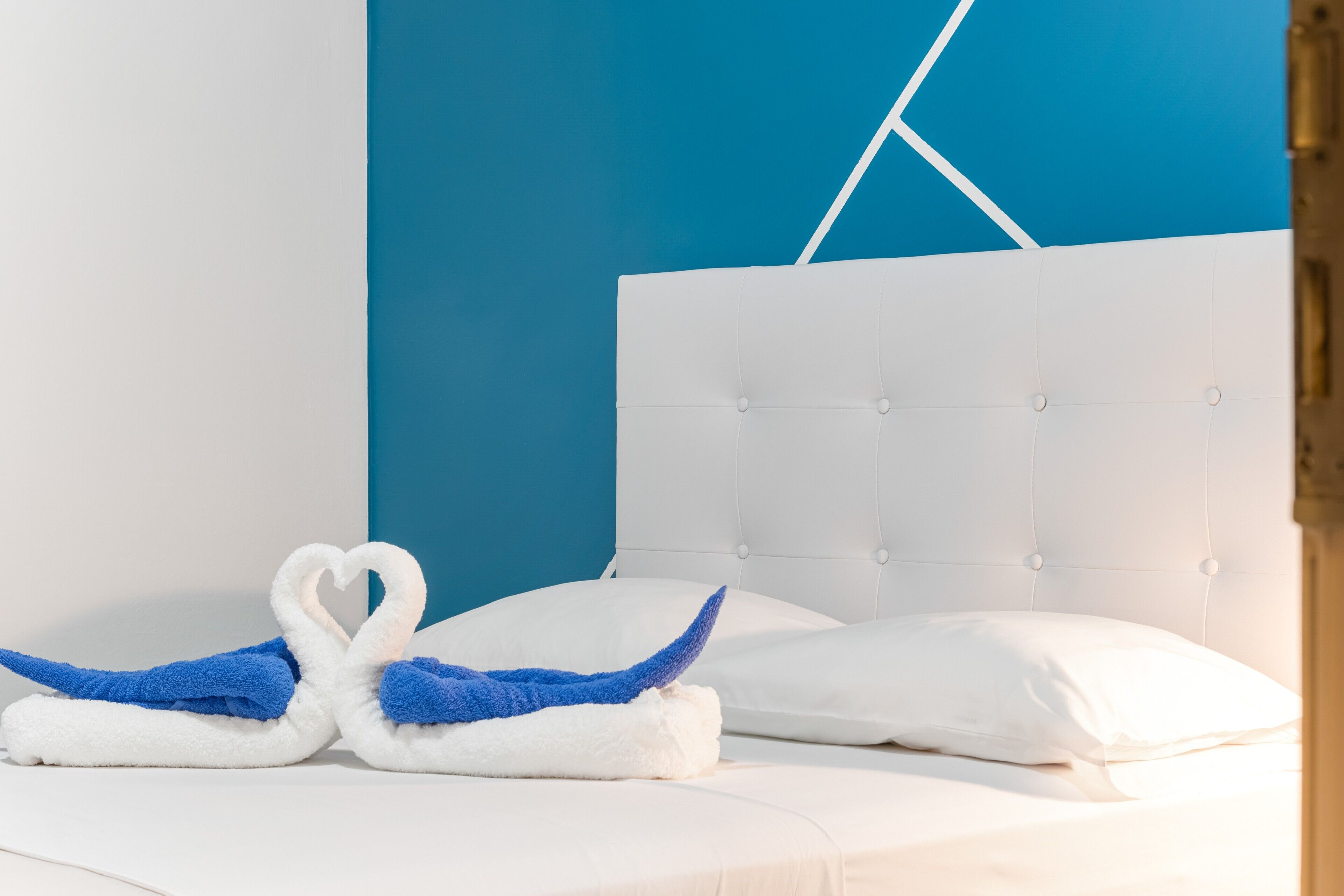 Un lit avec une literie blanche, un mur bleu et une tête de lit blanche.