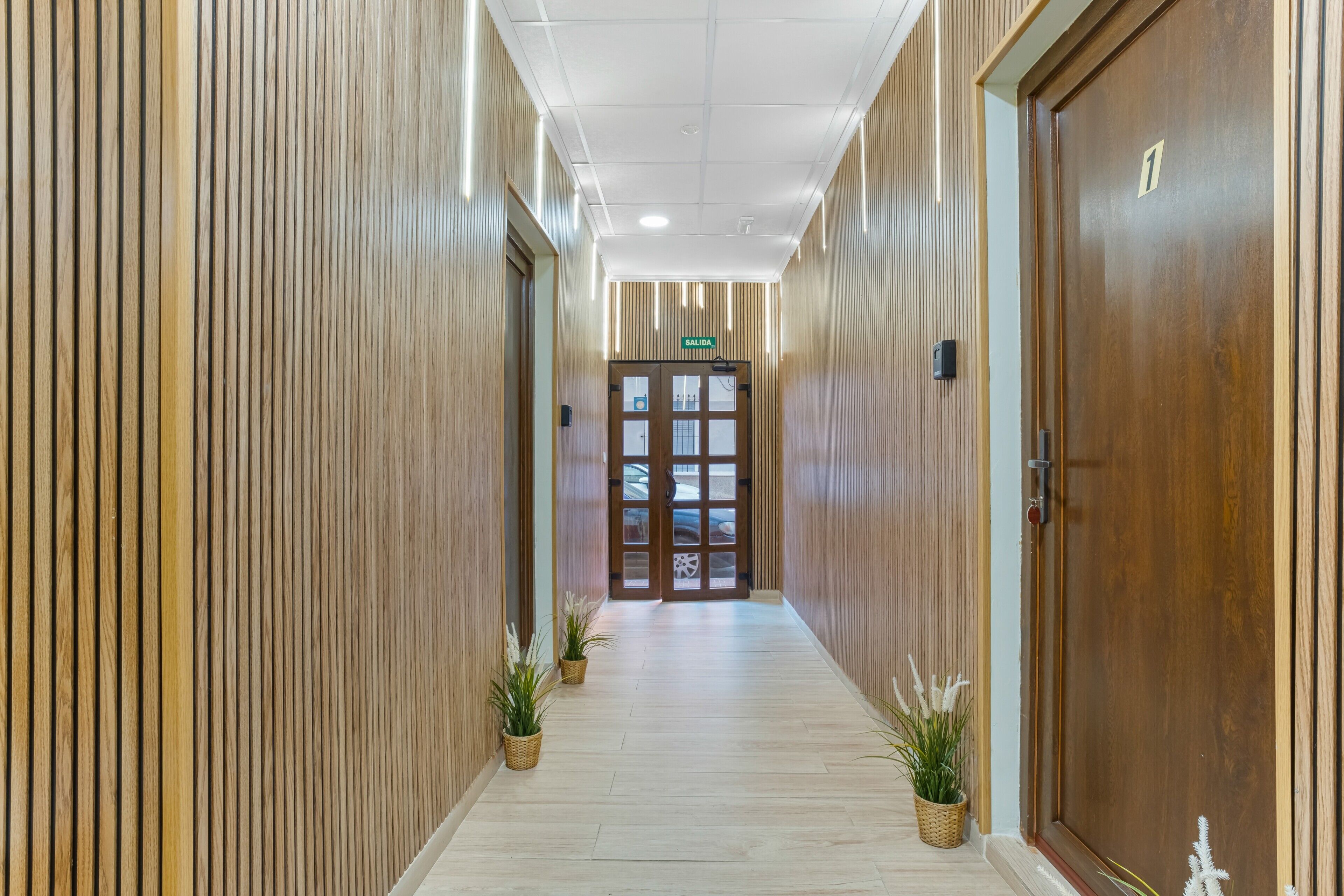 En hall med träpanel på väggarna, en dörr märkt med nummer 1 och krukväxter.