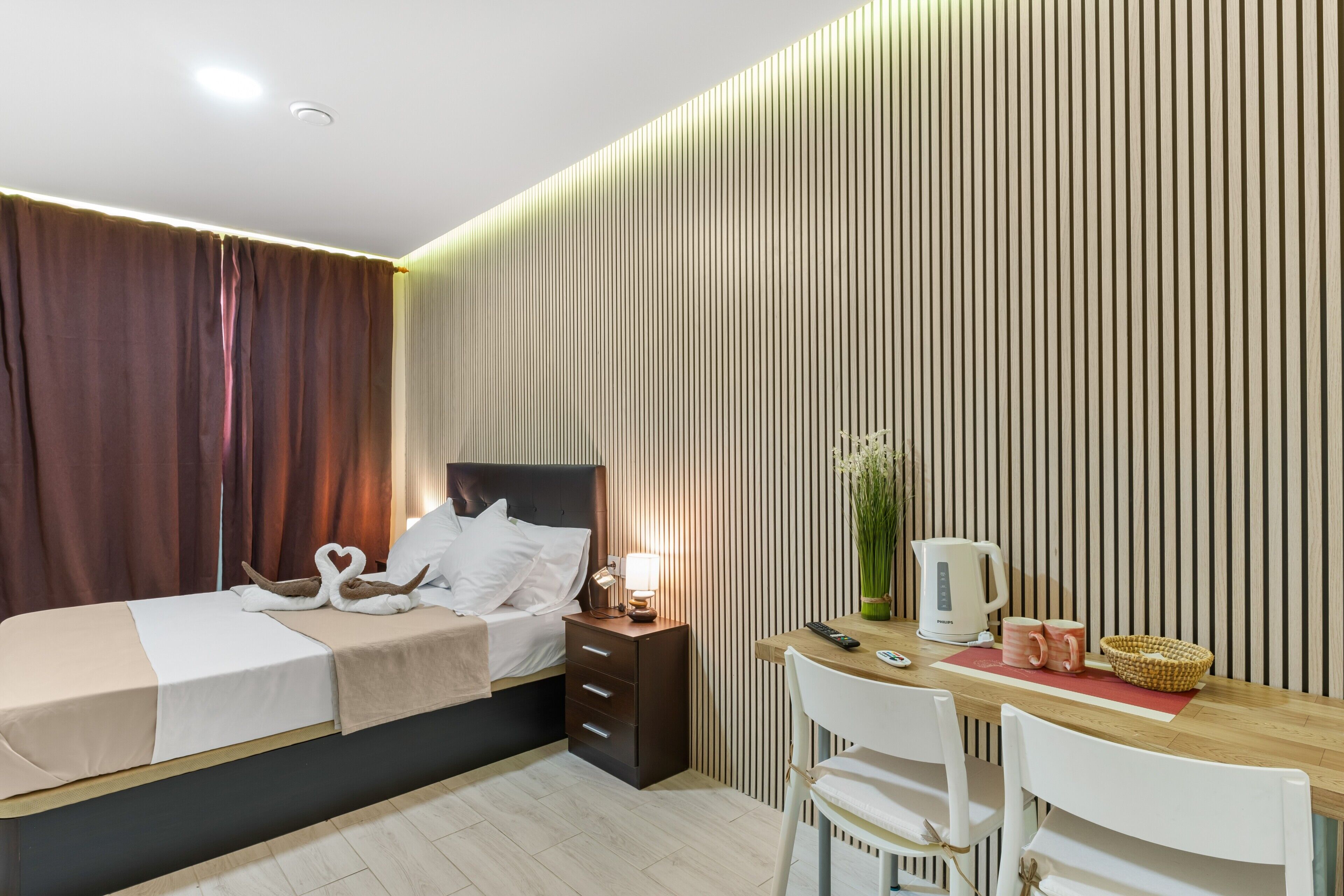 A hotel room with a bed, bedside table, lamp, and a desk with a chair.
