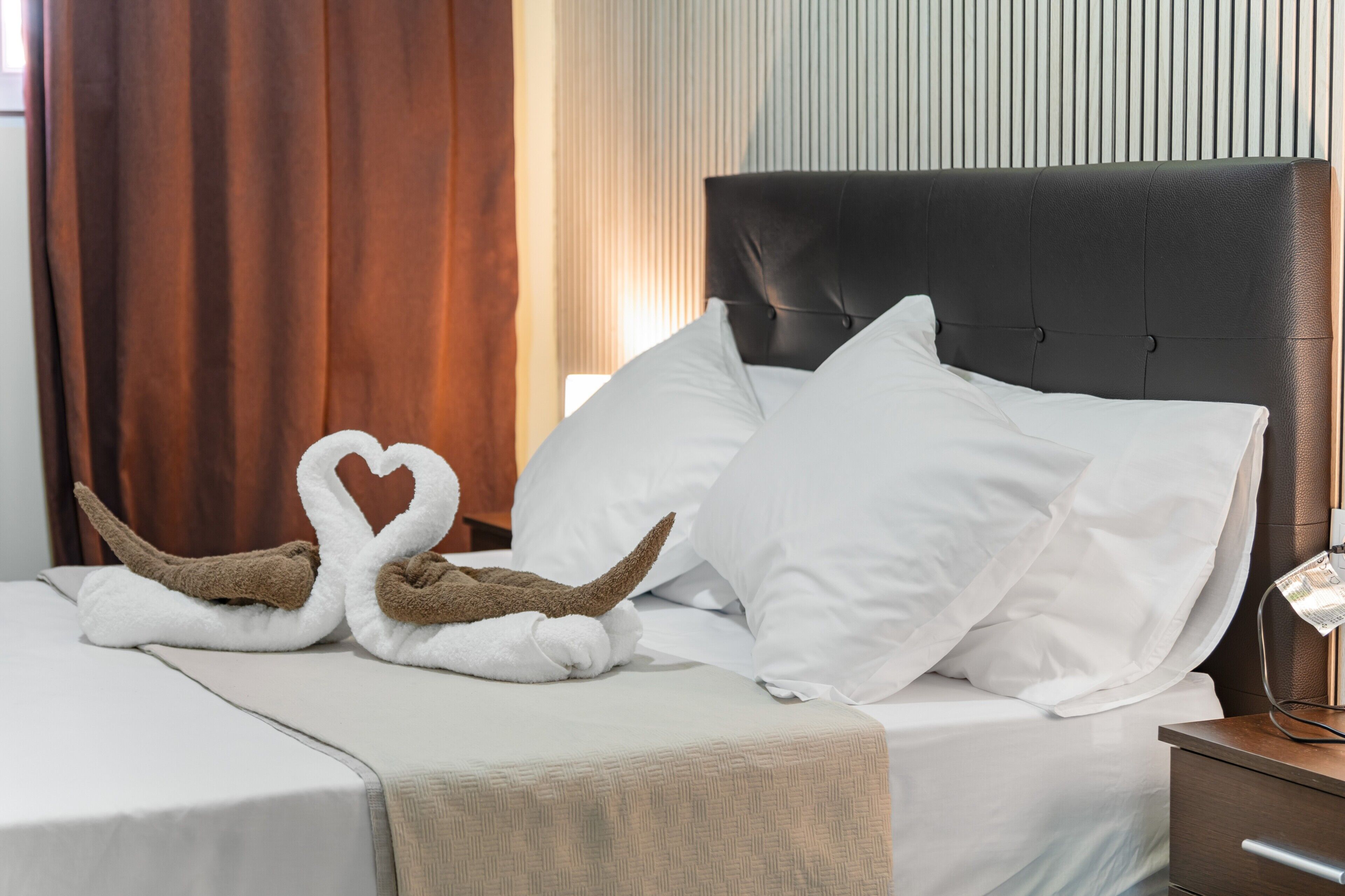 A neatly made bed with white linens, a headboard, and a bedside table with a lamp.