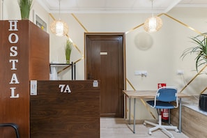 Hotellin vastaanottoalue, jossa on puinen vastaanottotiski, jossa lukee kyltti: »HOSTAL», sininen toimistotuoli, puinen työpöytä ja ovi, jossa on kyltti.
