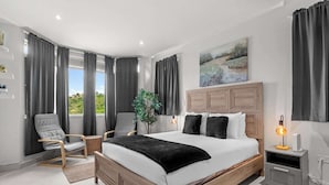 Una camera da letto moderna con un letto grande, tende grigie, una testiera in legno, un comodino con una lampada e vista su del verde all'esterno.