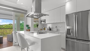 Una cucina moderna con una grande isola, elettrodomestici in acciaio inossidabile e vista su un balcone con mobili da esterno.