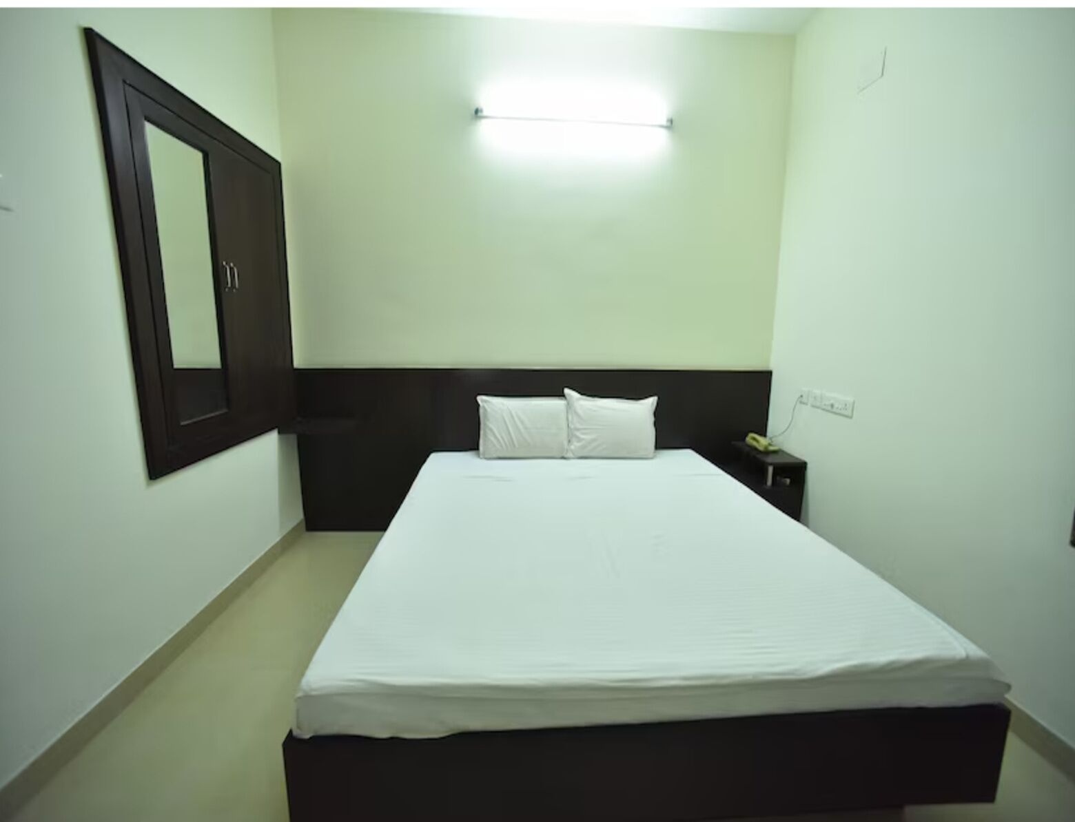 A standard hotel room with a bed, a nightstand, a wall-mounted mirror, and a ceiling light.