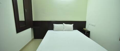 A standard hotel room with a bed, a nightstand, a wall-mounted mirror, and a ceiling light.