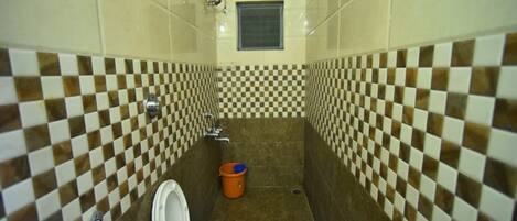 A bathroom with checkered tile walls, a toilet, a shower, and a window.