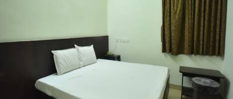A hotel room with a bed, a nightstand, a small table, and a curtain.