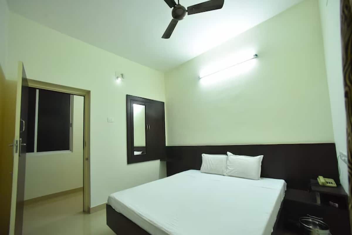 Una habitación de hotel con una cama, una mesita de noche, un teléfono, un ventilador de techo, una puerta y un espejo fijado a la pared.