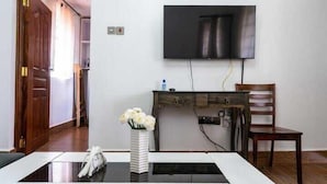 Une chambre dotée d’un téléviseur à écran plat fixé au mur, d’un bureau en bois avec une chaise, et d’un vase contenant des fleurs blanches, posé sur une table.