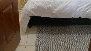 Un lit bien fait, avec une tête de lit noire, du linge de lit blanc et un tapis à motifs.