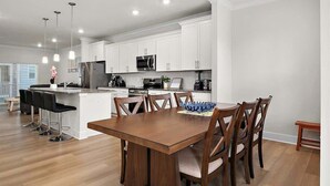 A modern kitchen with white cabinets, stainless steel appliances, and a central island with bar stools. - Z Estates | Balcony Beach View Townhome + Pool (Ocean City)