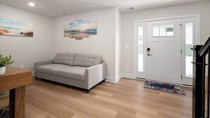 A living room with a grey sofa, wooden flooring, and a white door. - Z Estates | Balcony Beach View Townhome + Pool (Ocean City)