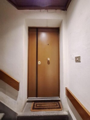 Puerta de madera con picaporte metálico y cerradura, en un pasillo con paredes blancas y zócalo de madera.