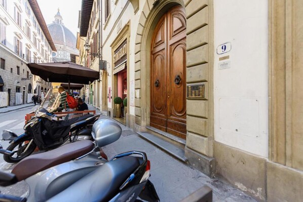 Une rue bordée de scooters garés et une grande porte en bois portant le numéro 9.