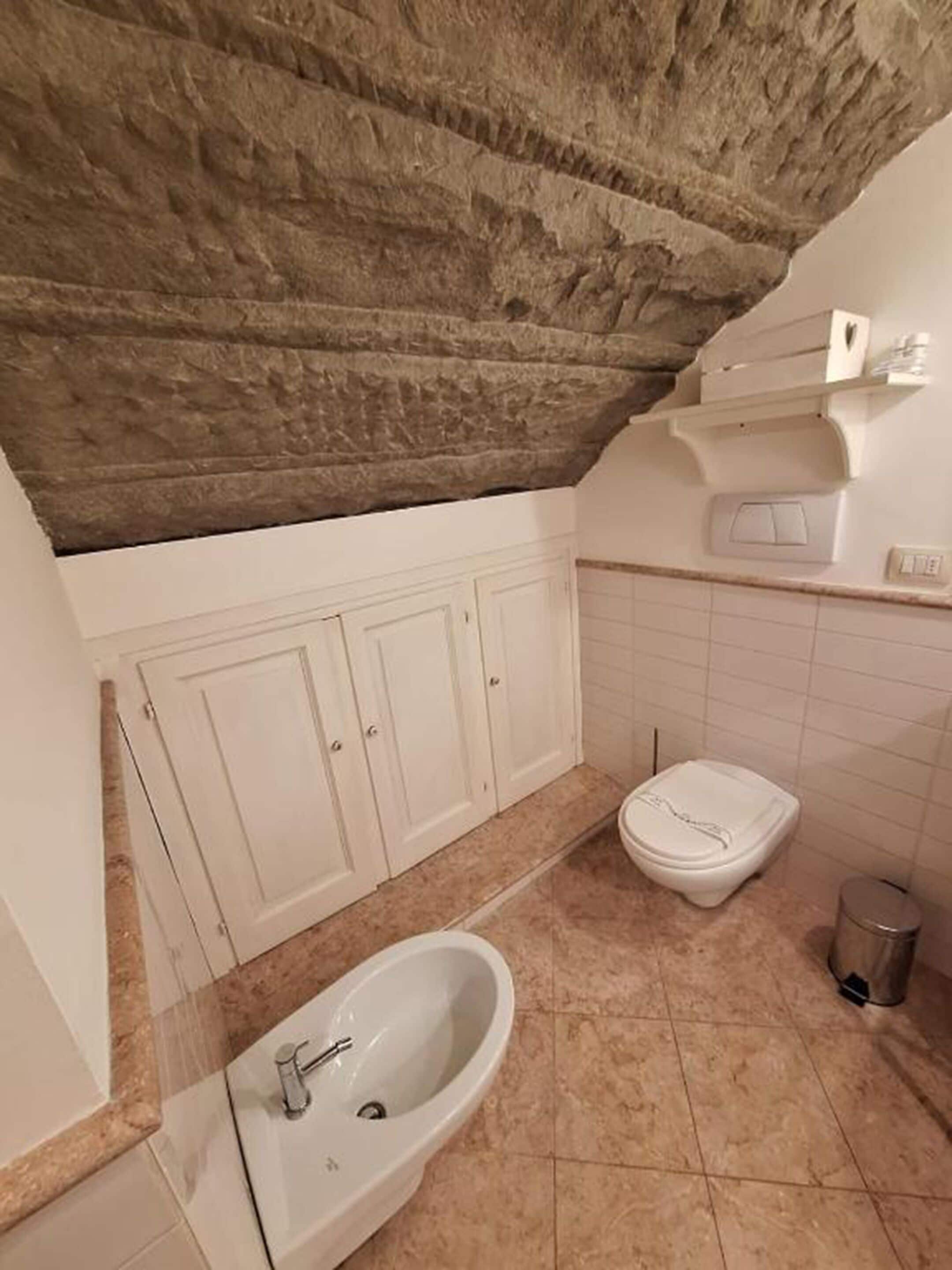 Un baño con techo de piedra, un lavabo blanco, un inodoro y un cubo de basura.