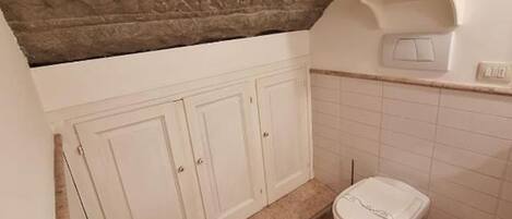 Un baño con techo de piedra, un lavabo blanco, un inodoro y un cubo de basura.