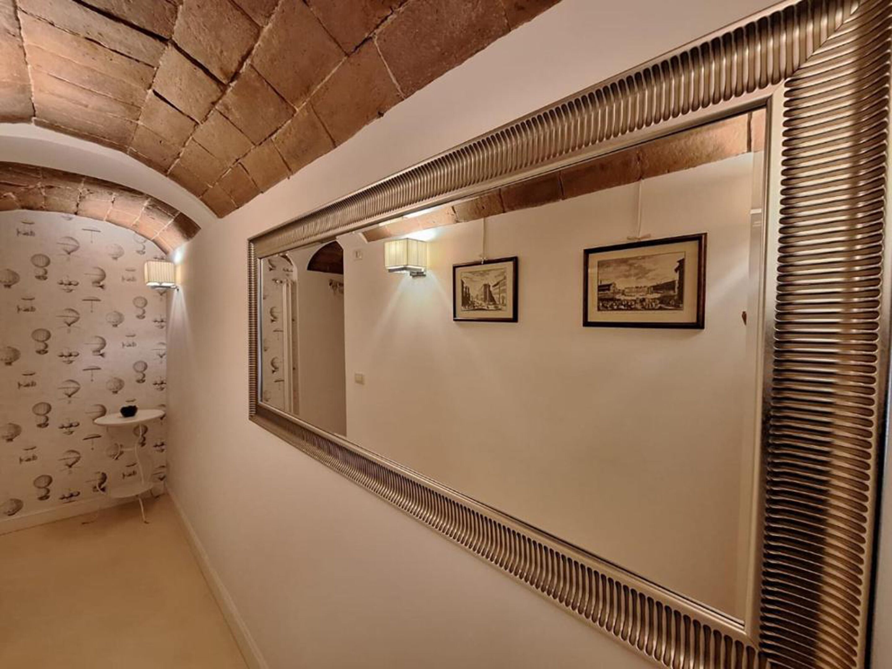 Un couloir avec un grand miroir, un lavabo et deux tableaux encadrés accrochés au mur.