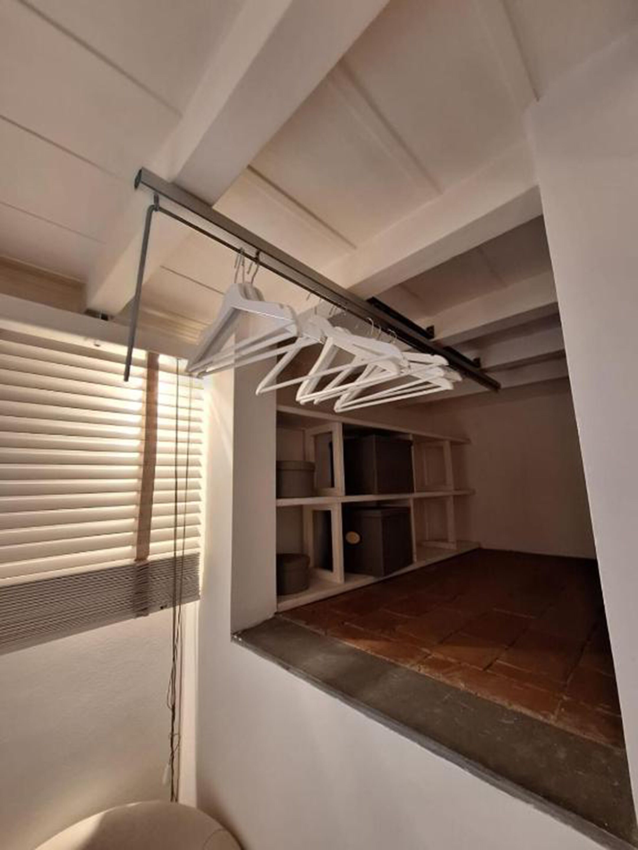 Ein Zimmer mit integriertem Bücherregal, einer Kleiderstange und einem Fenster mit Jalousien.
