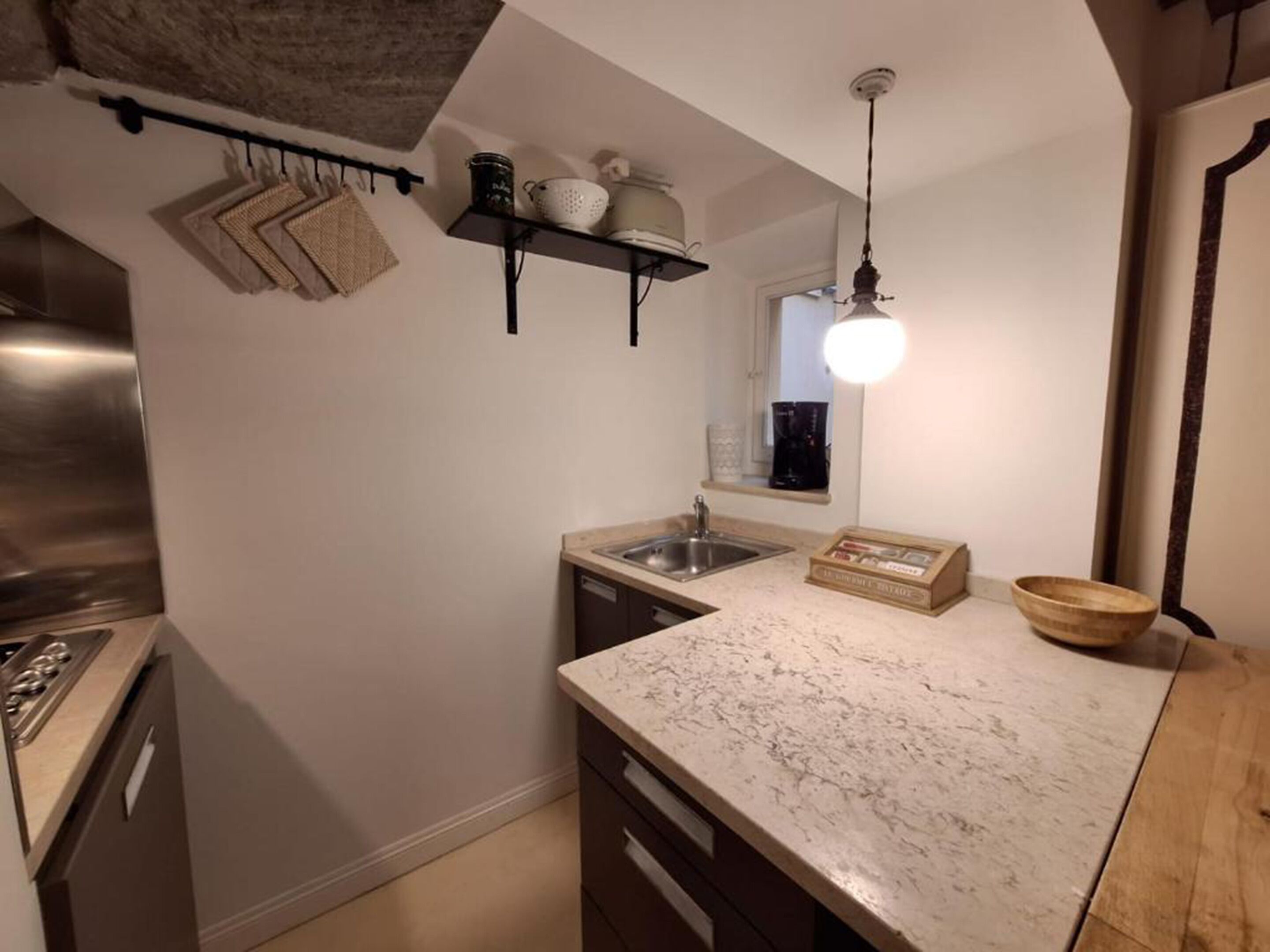 A compact kitchen with a marble countertop, a built-in sink, and a hanging pot rack.
