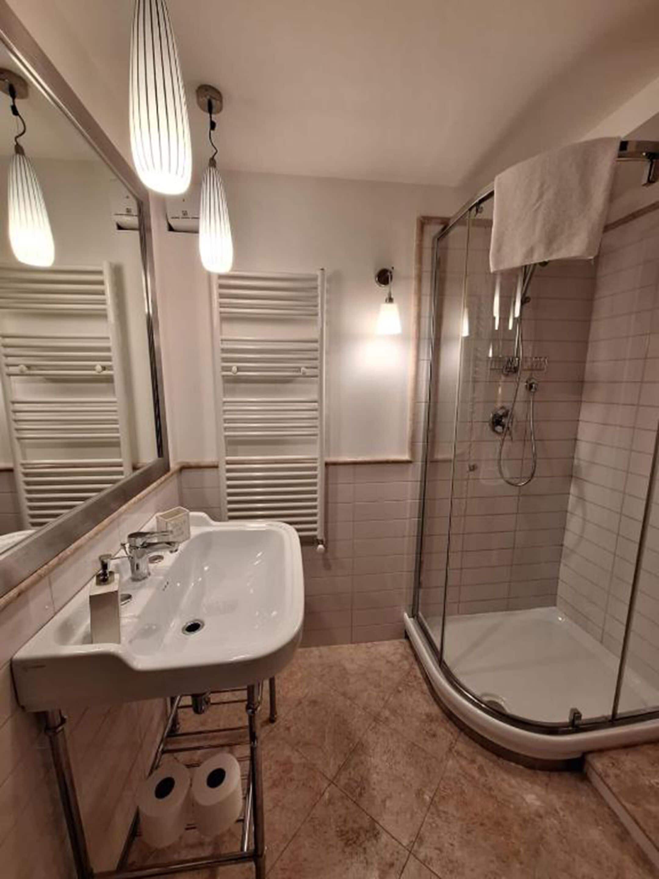 Une salle de bain avec un lavabo blanc, une cabine de douche en verre et une serviette accrochée à la porte de la douche.