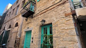 Ein Gebäude aus Stein mit grünen Fensterläden, einem Balkon mit schmiedeeisernem Geländer und Topfpflanzen im Erdgeschoss.