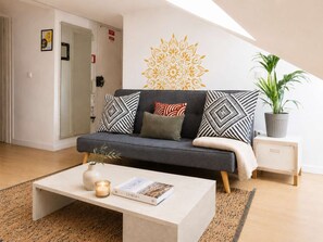 A modern living room with a sofa, a coffee table, a potted plant, and a decorative wall piece. - Sunset Terrace Retreat | Tagus Views & LX Factory (Lisbon)
