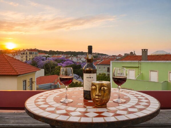 Une table avec une bouteille de vin et deux verres sur un balcon donnant sur une vue panoramique de la ville au coucher du soleil.