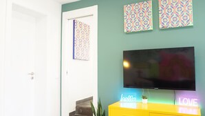 Een kamer met een televisie, een geel kastje, een trap en decoratieve wandkunst met een patroon.