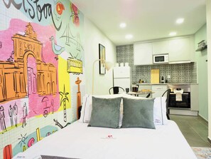 A hotel room with a bed, pillows, a wall mural, a small kitchen area with a microwave, and a sink. - Ground-Floor 1BR Merces• Chiado •  Tram 28 (Lisboa)