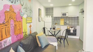 Een moderne woonkamer met een bank, stoelen, een eettafel en een keuken met witte kasten en een magnetron.