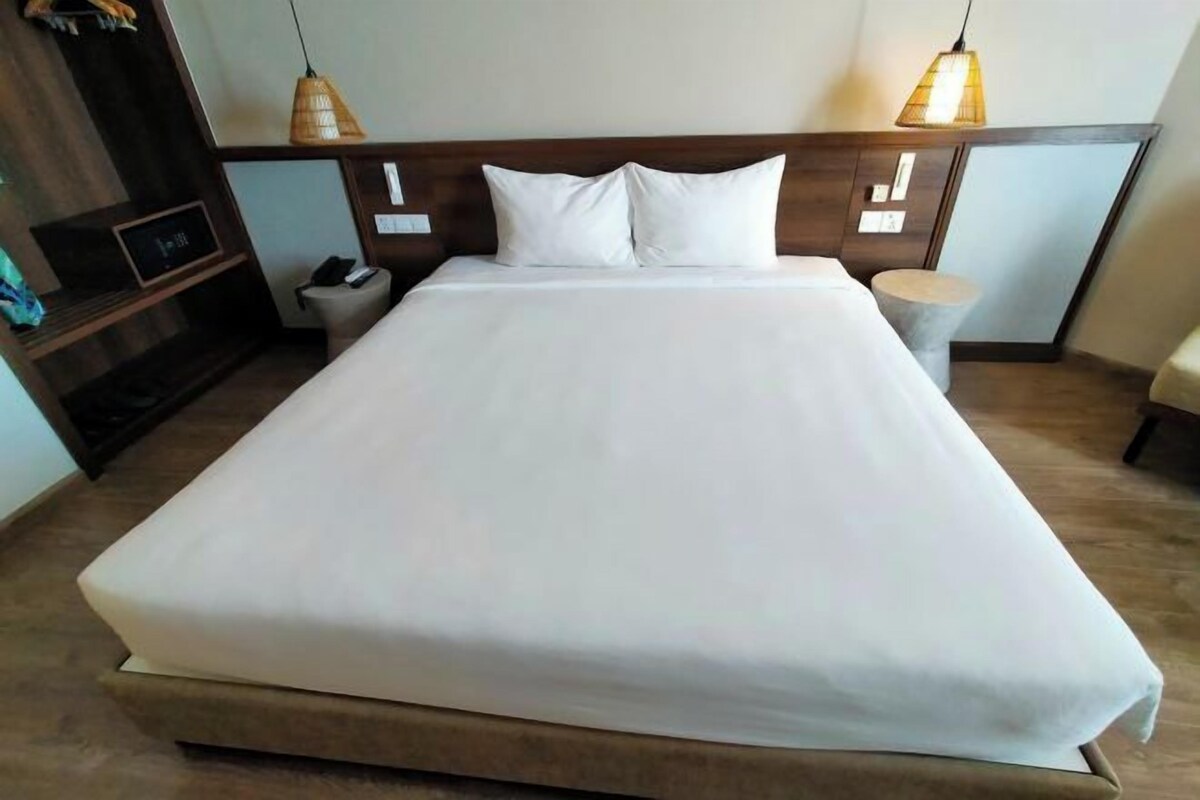 Un grand lit avec du linge de lit blanc, une tête de lit en bois, des tables de chevet et deux lampes suspendues.