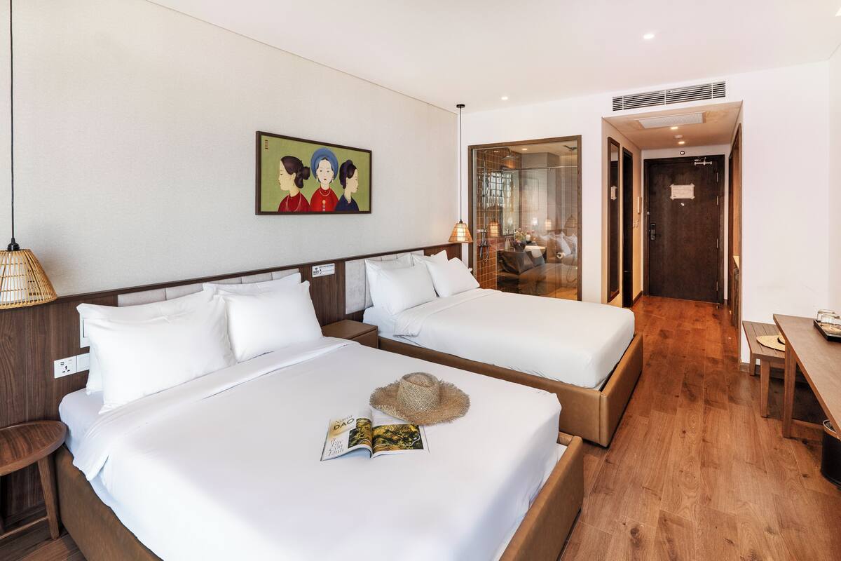 Une chambre d’hôtel avec deux lits, un plancher en bois, un tableau au mur et une salle de bain visible à travers une porte en verre.
