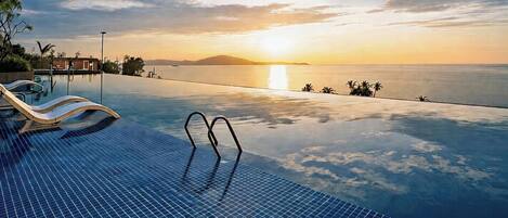 An infinity pool with lounge chairs and a sunset view.